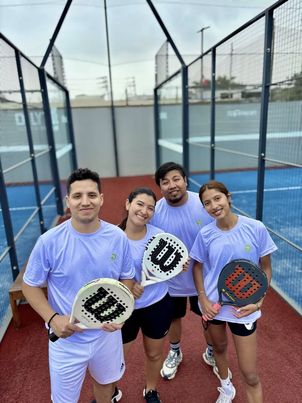 Cuatro jugadores con polos Padelhood y raquetas en la cancha
